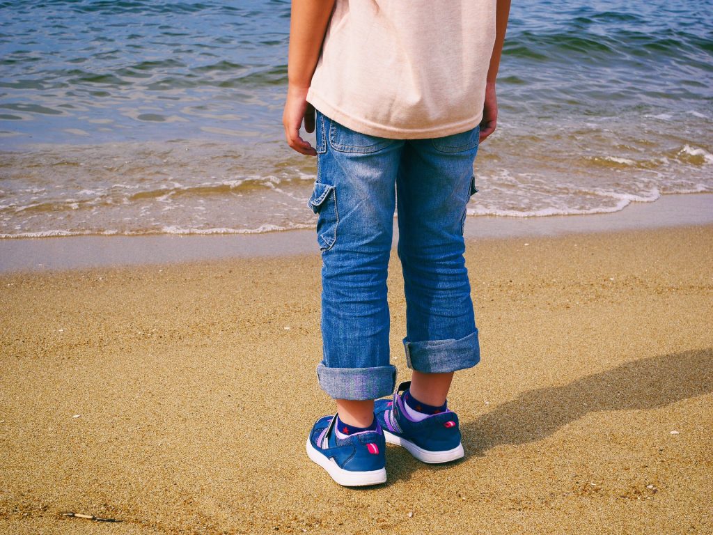 海を前に砂浜に立つ男の子の後ろ姿